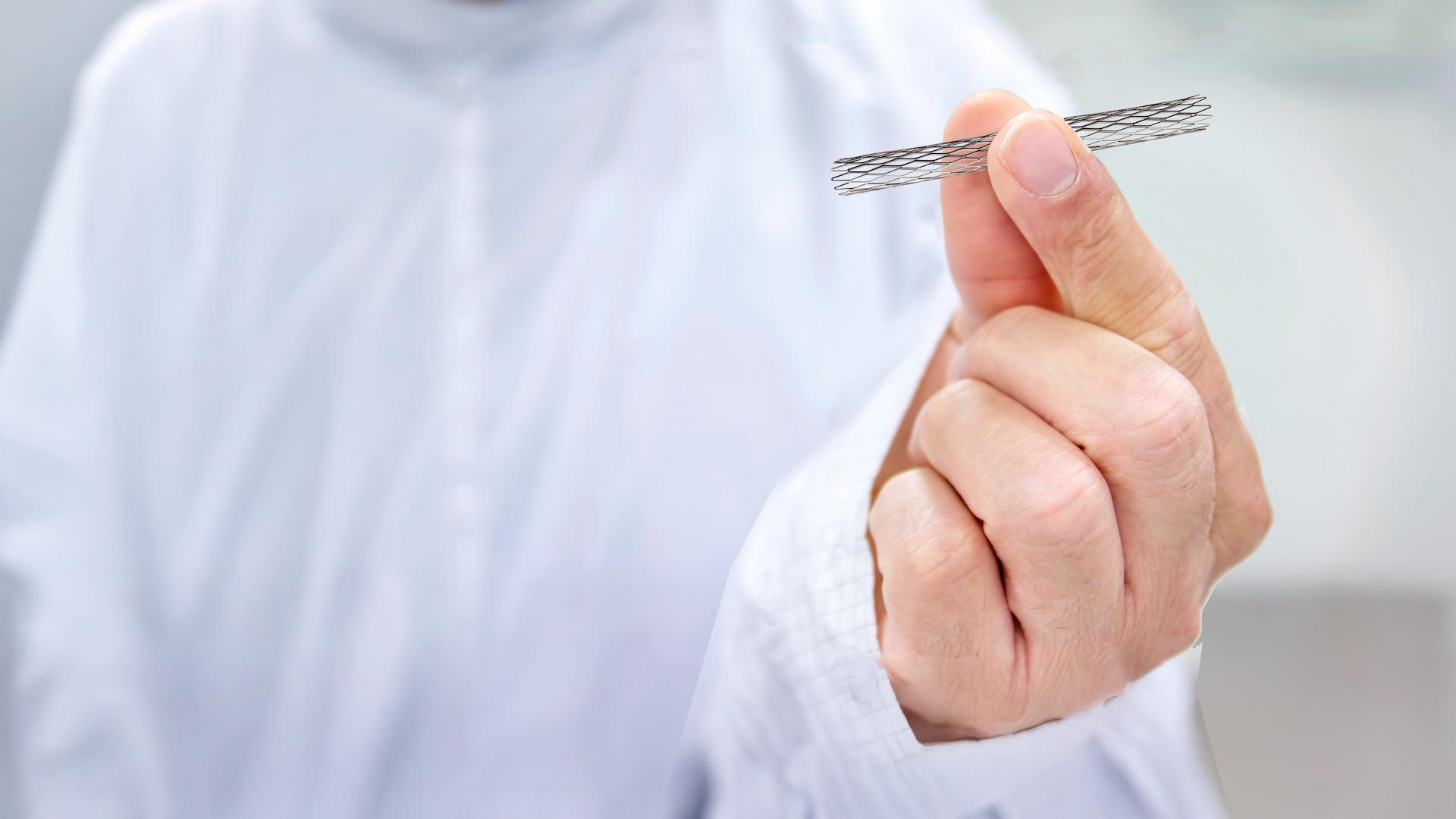 A person in a white lab coat holds a small, cylindrical medical stent between their fingers in a clean, clinical environment.