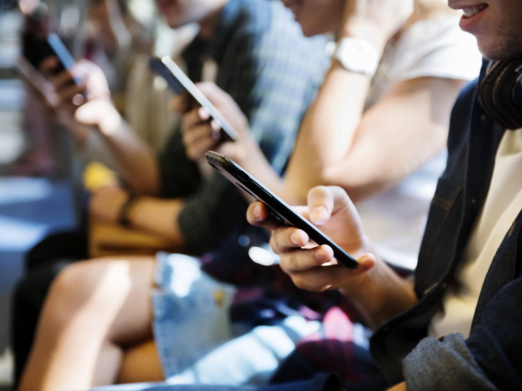 Smartphone-urile emit niveluri ridicate de lumină albastră. În imagine sunt mai multe persoane care se uită la smartphone-uri. 