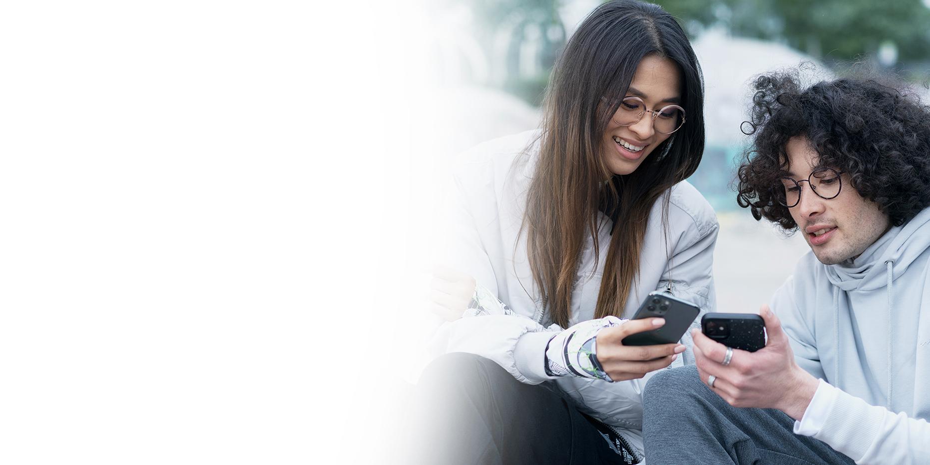 Doi tineri, o femeie cu părul șaten lung, care zâmbește, și un băiat cu părul negru și creț care poartă ochelari ZEISS SmartLife, uitându-se la telefoanele lor. 