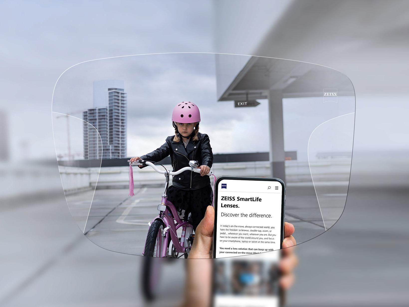 Persoană care se uită la telefon prin lentilele progresive ZEISS SmartLife. În fundal se vede o fată pe bicicletă, cu cască roz de protecție pe cap. 