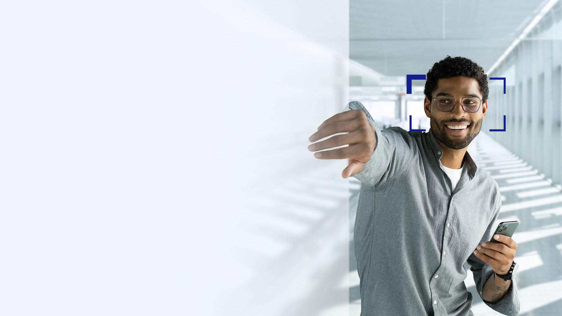 Un tânăr cu păr negru care zâmbește și își întinde mâna prin ecran, în timp ce poartă lentile ZEISS SmartLife.