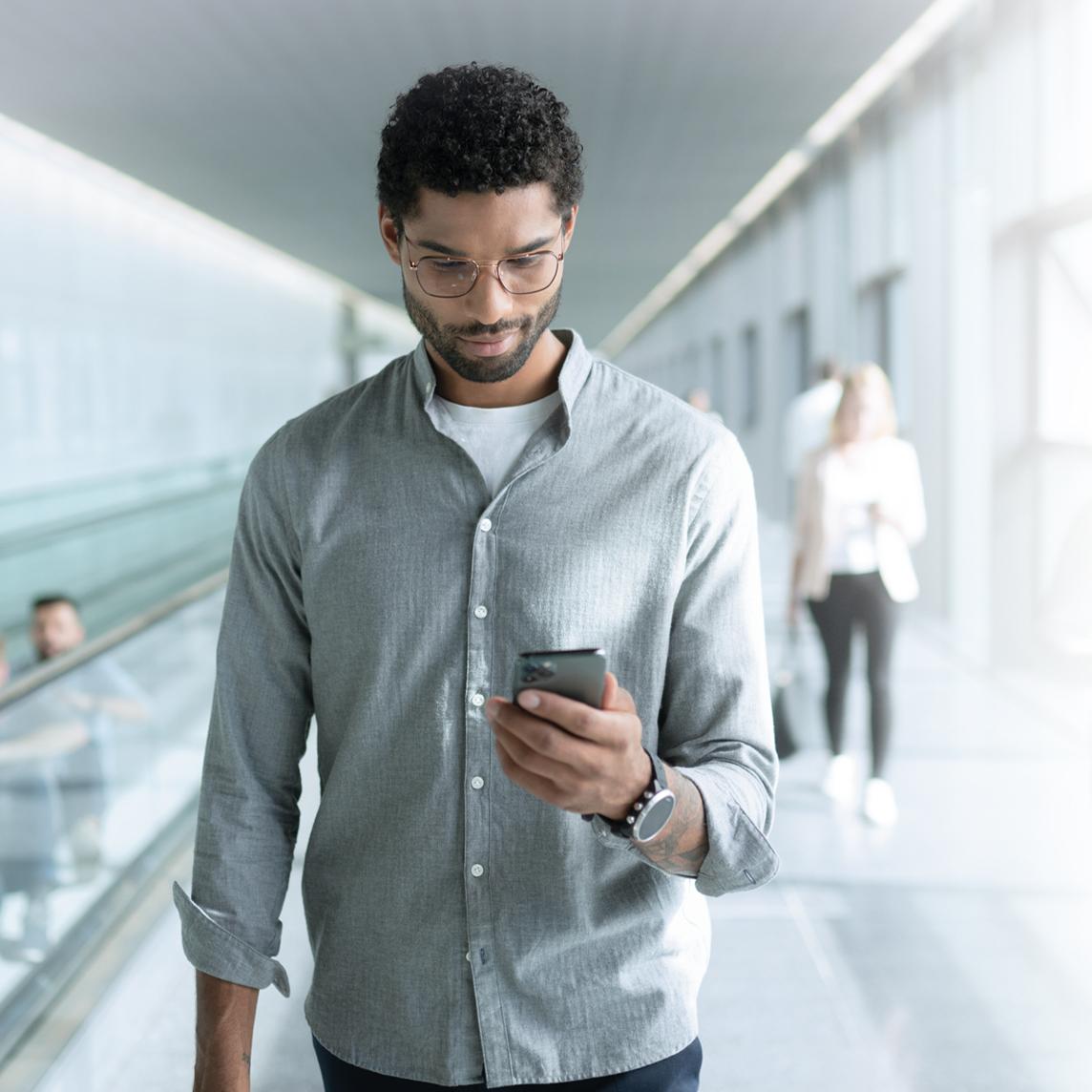 Tânăr care poartă lentile ZEISS SmartLife și se uită la telefon în timp ce merge.