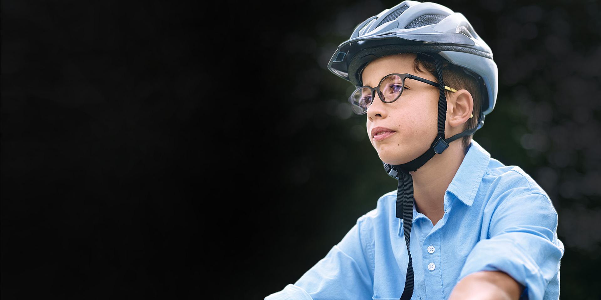 Un băiat care poartă ochelari și o cască de protecție apare mergând pe bicicletă.