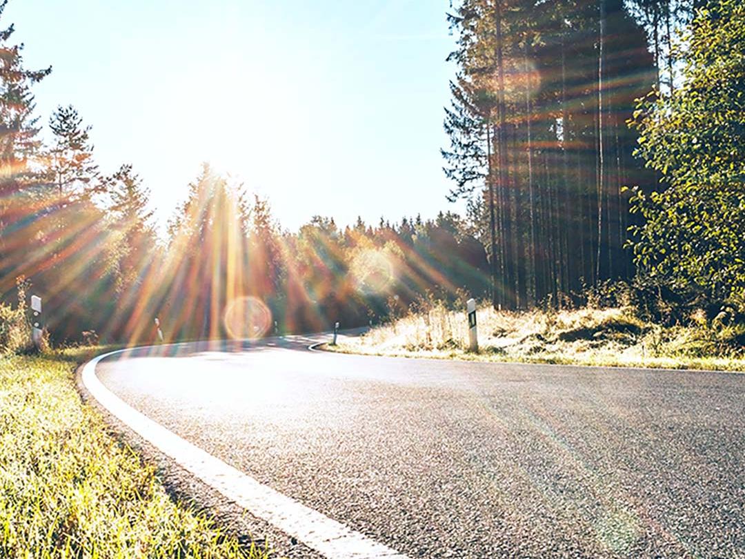 O imagine glisantă în care o jumătate arată un drum în pădure cu lumină puternică de la soare, iar cealaltă jumătate arată același drum cu strălucire redusă și contrast sporit, evidențiind efectul lentilelor de ochelari de soare polarizați.