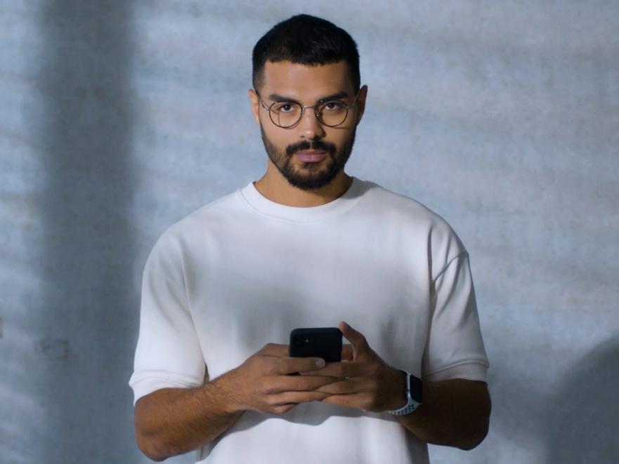 Un tânăr care poartă ochelari cu lentile BlueGuard, ocupat cu smartphone-ul său