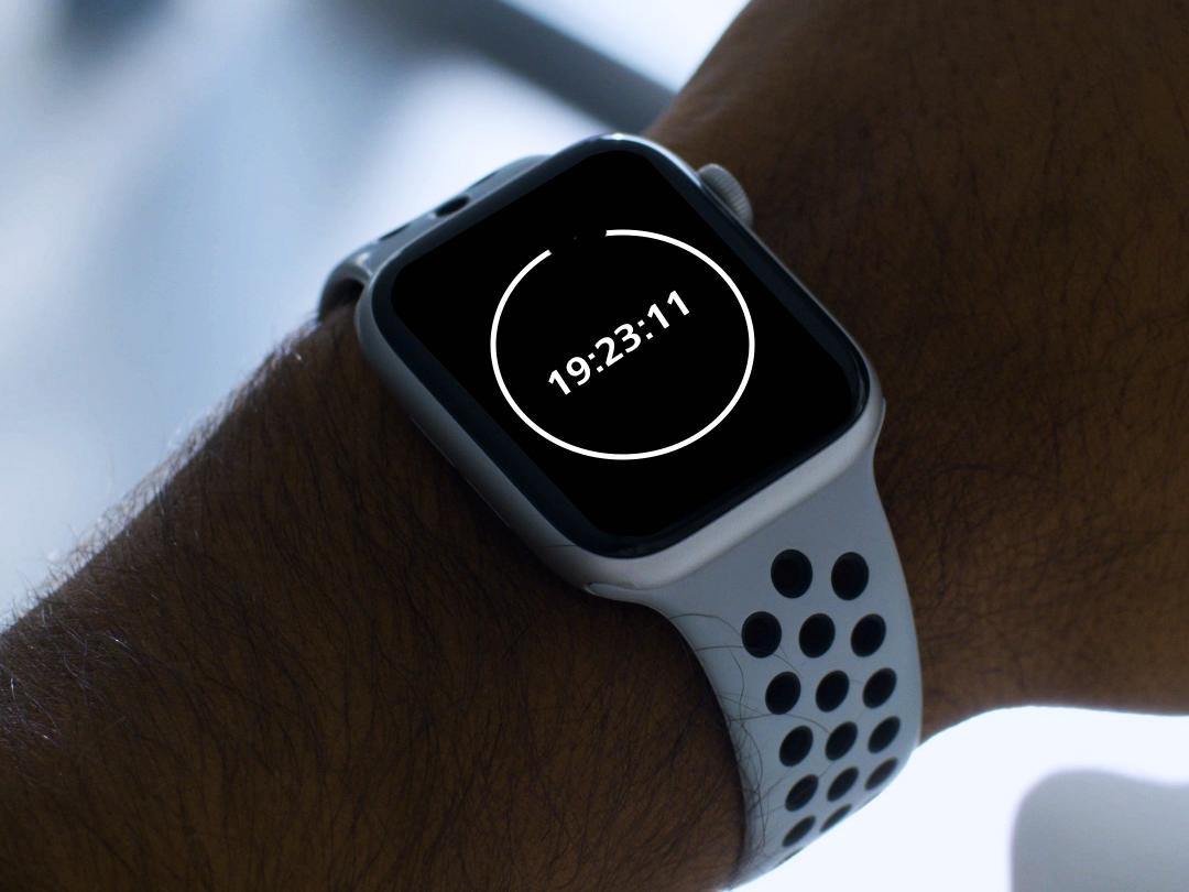 Un tânăr care poartă ochelari cu lentile BlueGuard, privind în jos la smartwatch-ul său care arată un cronometru de 20 de minute.  