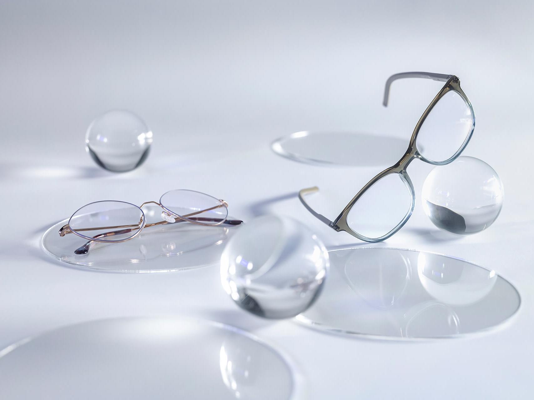 Ochelari cu lentile ZEISS care au tratament DuraVision® Silver și nu prezintă reflexii în comparație cu sferele de sticlă din jur.