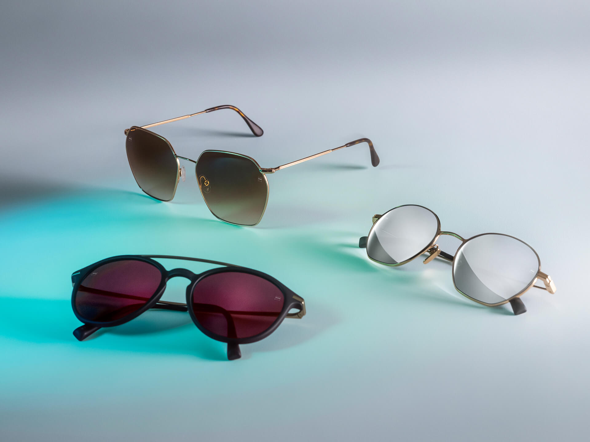 Trei perechi de ochelari de soare cu lentile ZEISS de diferite culori, cu tratamente DuraVision Sun, DuraVision Mirror și Flash Mirror, vizibile pe un fundal alb cu reflexii de lumină albastră.