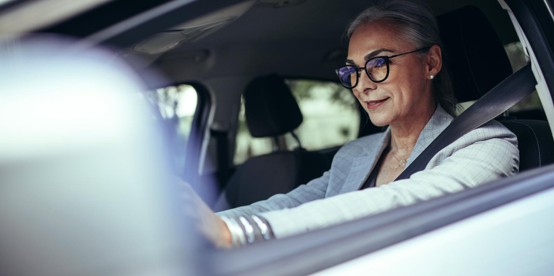 O femeie matură în mașină care poartă ochelari cu lentile ZEISS DriveSafe.