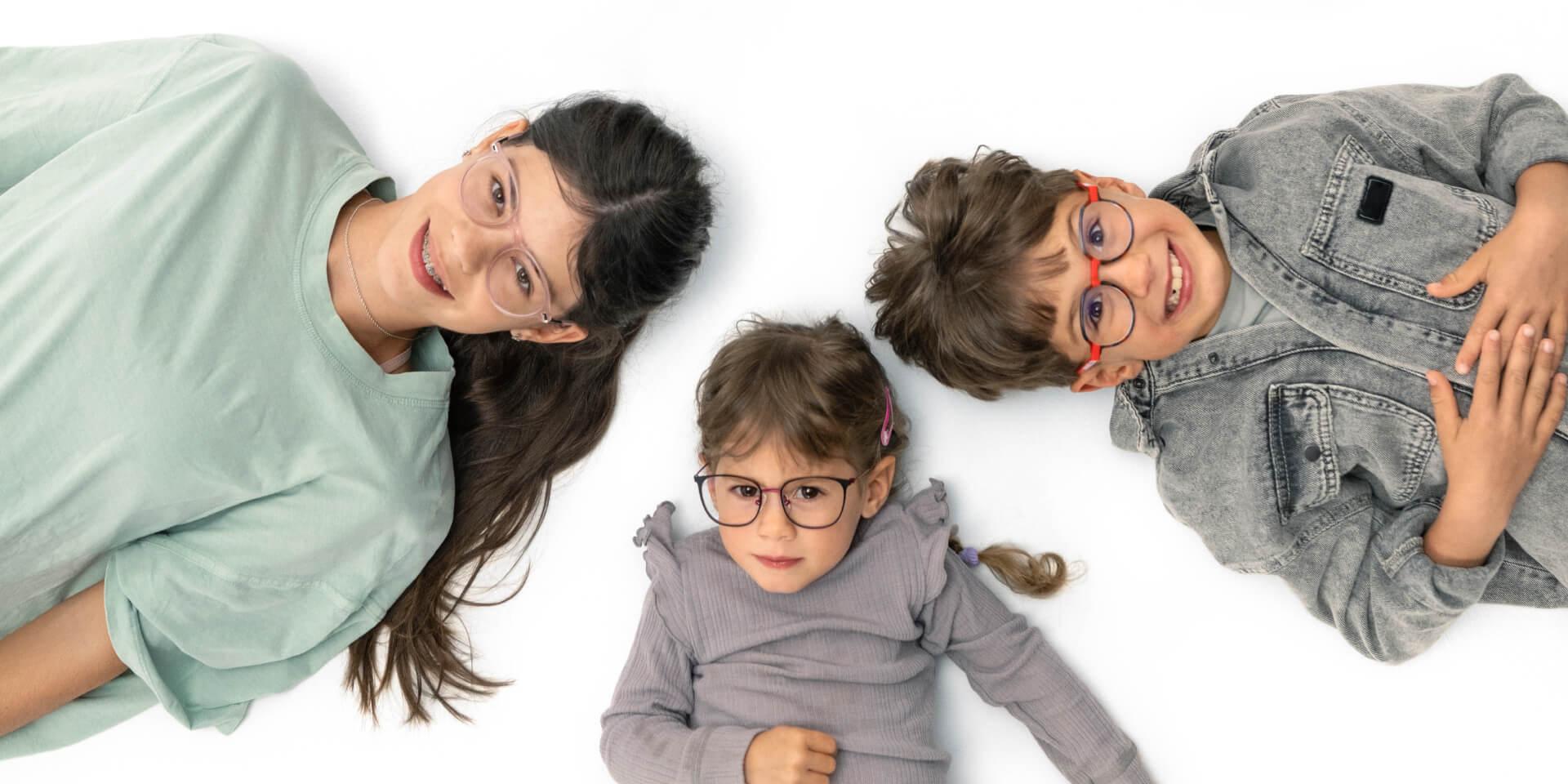 Un adolescent și doi copii mai mici stau pe podea purtând lentile ZEISS pentru miopie