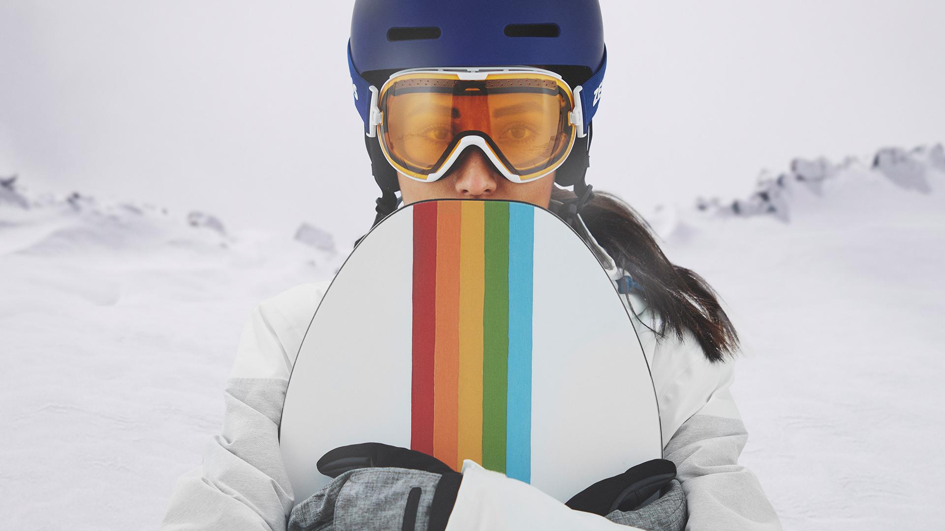 O tânără care poartă ochelari de protecție pentru schi cu tehnologie ZEISS interschimbabilă și care ține un snowboard.