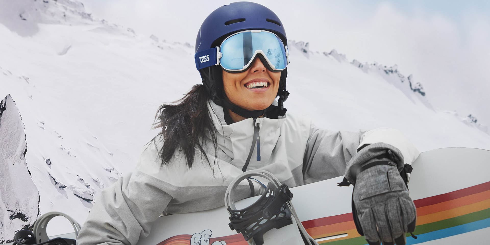 O tânără care poartă ochelari de protecție pentru zăpadă cu tehnologie ZEISS interschimbabilă și ține un snowboard.
