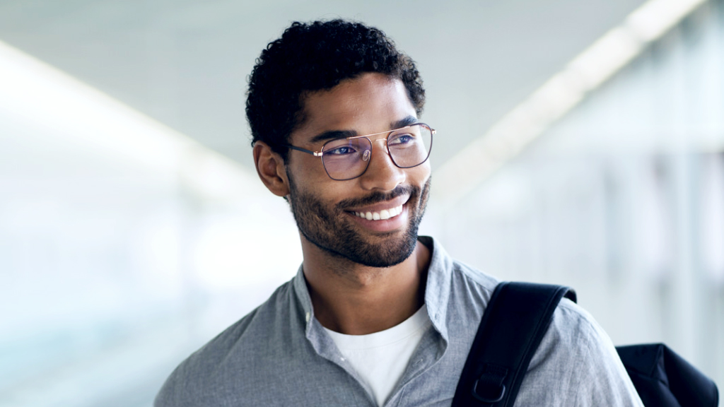 Un tânăr zâmbind, cu un rucsac peste umăr, poartă ochelari ZEISS SmartLife Digital și privește în lateral.
